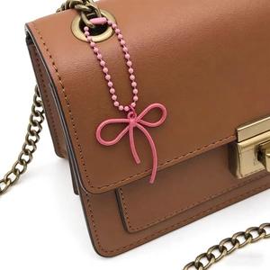 Detailed close-up of pink lacquer bow pendant on beaded chain attached to leather bag