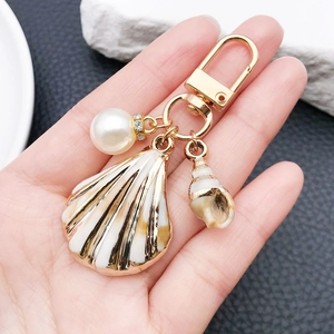 Detail of seashell keychain with enamel scallop pendant, conch charm and pearl in hand