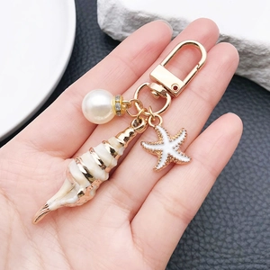 Detail of marine keychain with golden shell, white starfish, and pearl on gold ring