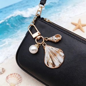 Detail of seashell and pearl keychain hanging on a premium black textured leather bag