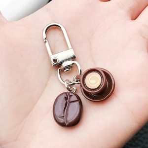 Detail of coffee bean and latte art cup charm keychain held in hand for scale