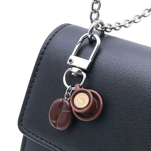 Detail of coffee cup and bean keychain hanging on a black leather bag for decoration