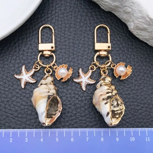 Détail de deux porte-clés de style océan avec coquillage et étoile de mer sur fond noir