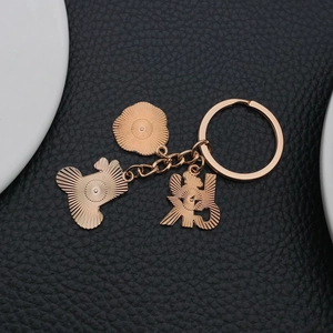 Detail of rose gold clover keychain with elephant and sun charms on leather background