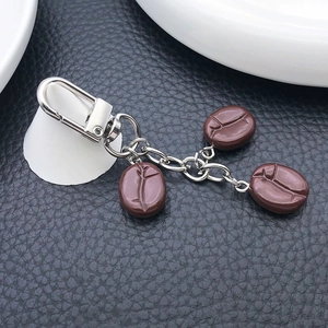 Creative coffee bean resin keychain with silver U-shape spring clasp on black leather background