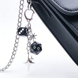 Detail of a black dice keychain with star charms and silver chain on a leather bag