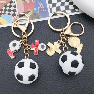 3D soccer ball keychain with metallic ring and red shoe charm on black leather background