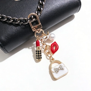 Detail of golden alloy keychain with red lips, lipstick, pearl and white handbag charms