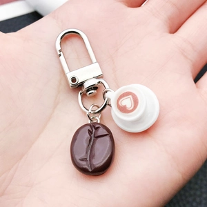 Close-up of resin coffee bean and heart latte art cup keychain held in hand