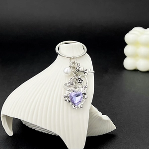 Détail d'un porte-clés cœur en cristal violet et rose en métal sur un support blanc