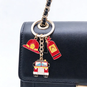 Detail of firefighter themed keychain with helmet and extinguisher charms on black leather bag