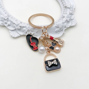 Détail de porte-clés doré avec sac à main noir, perles et pendentif rouge à lèvres