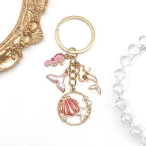 Detail of pink enamel ocean charms including seahorse and mermaid on golden keychain