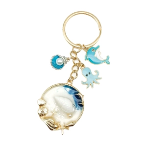 Dettaglio di un portachiavi oceano blu con ciondoli dorati di delfino e conchiglia e perle