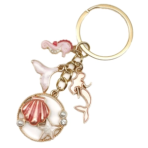 Detailed macro view of pink enamel seahorse and mermaid tail charms on golden keychain