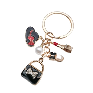 Détail d'un porte-clés doré avec sac à main noir, perle et charms de rouge à lèvres