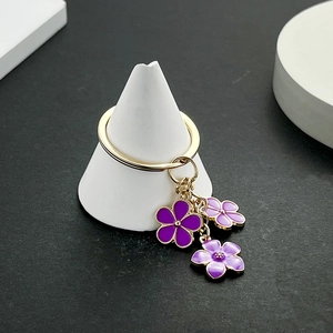 Détail de trois breloques fleurs de cerisier en émail violet sur un anneau doré