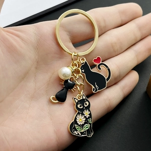 Porte-clés doré avec trois pendentifs chats en émail noir et une perle élégante