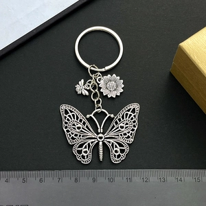 Antique silver butterfly keychain with bee and sunflower charms on a black background