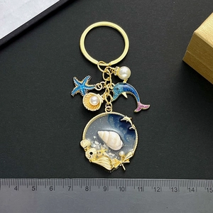 Blue ocean keychain featuring starfish, pearl shell, and dolphin charms on gold ring