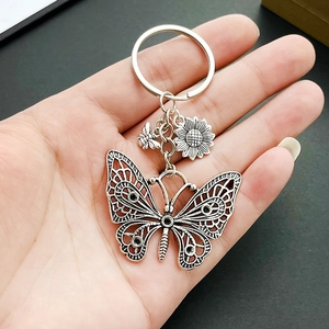 Antique silver hollow butterfly keychain with sunflower and bee charms held in hand