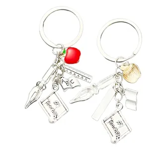 Silver teacher keychain with red apple, ruler and book charms on white background
