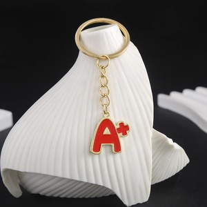 Detailed macro view of a gold-toned keychain featuring a red enamel A+ charm and a metal ring