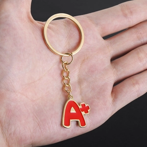 Golden A+ letter keychain with red enamel drip oil finish held against black background