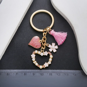 Pink heart keychain with tassel, pearl flower charm, and size ruler on black background