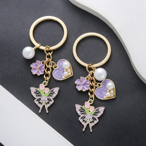 Golden keychain with purple tulip, butterfly, and pearl heart pendant on a modern background