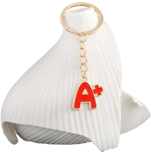 Golden A+ letter keychain with red enamel charm hanging on white ceramic holder