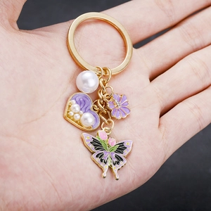 Detail of purple tulip butterfly keychain with heart pendant and pearl held in hand