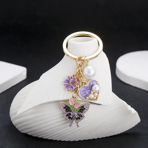 Detailed shot of purple enamel flower, pearl heart, and tulip butterfly charms on gold keychain