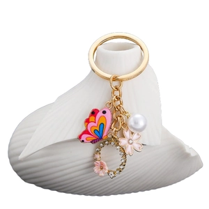 Portachiavi dorato con farfalla rosa e perla e ciondoli a fiore smaltati su sfondo bianco