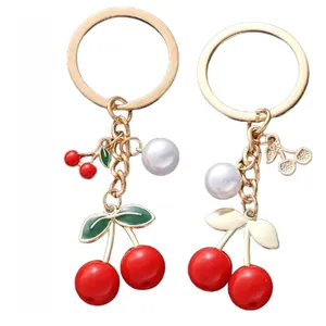 Detail of red cherry pendant keychain with gold chain, green leaves and white pearl