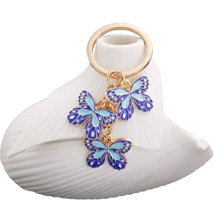 Golden butterfly keychain with three blue enamel charms on a white ceramic display
