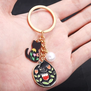 Porte-clés doré avec chats en émail noir, fleurs colorées et perle tenu en main