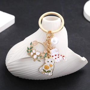 Detail of a golden cat keychain with white enamel flowers, heart motif and faux pearl charm