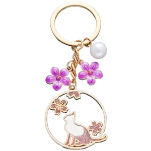 Détail d'un porte-clés chat doré avec fleurs de cerisier en émail violet et perle