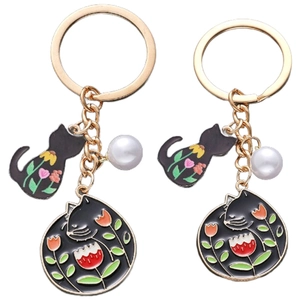 Détail de porte-clés chat noir avec fleurs en émail et pendentif perle en métal doré