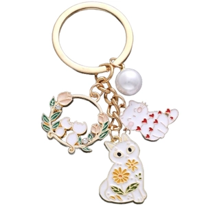 Detail of a cat keychain with white enamel cats, tulip wreath, and a large pearl charm