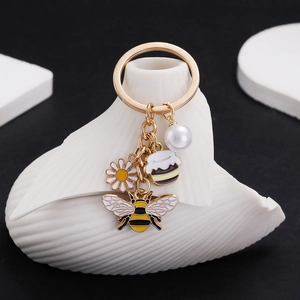 Porte-clés abeille et marguerite avec perle et pendentifs dorés sur fond élégant