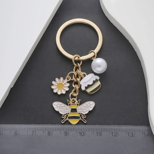 Détail des charms abeille, marguerite et perle sur porte-clés avec règle de mesure en cm