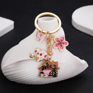 Pink enamel mushroom house flower and butterfly gold keychain on white wavy ceramic pedestal
