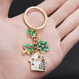 Detailed view of enamel keychain with mushroom, butterfly, and cottage charms on a hand
