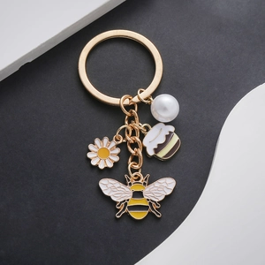 Vue détaillée du porte-clés doré avec charms abeille, fleur de marguerite et perle