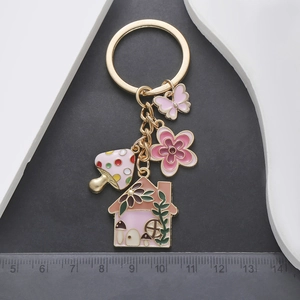 Detail of pink mushroom house and flower alloy charms on a gold keychain pendant