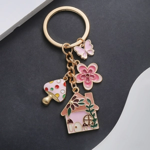 Detail of pink enamel charms featuring a mushroom house, flower, and butterfly keychain