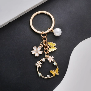 Detail of golden floral keychain with yellow butterfly charm and pearl on black backdrop
