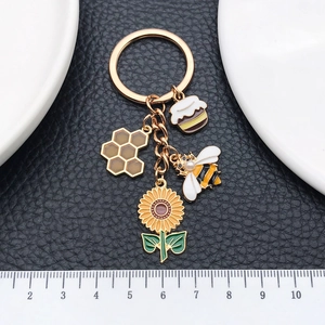 Golden keychain with sunflower bee and honeycomb enamel charms on black leather background